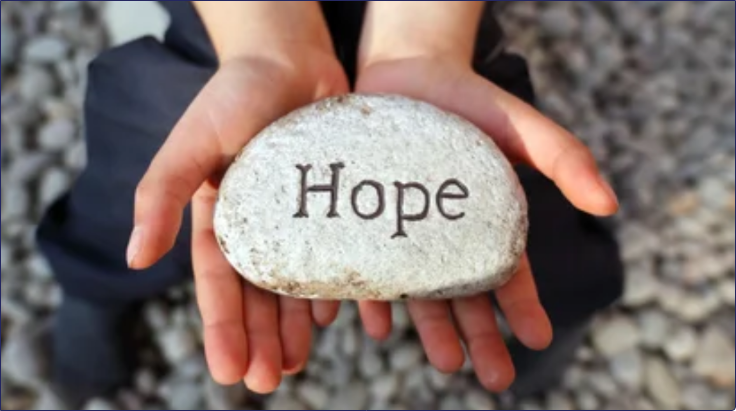 two hands holding flat large stone with the word hope inscribed